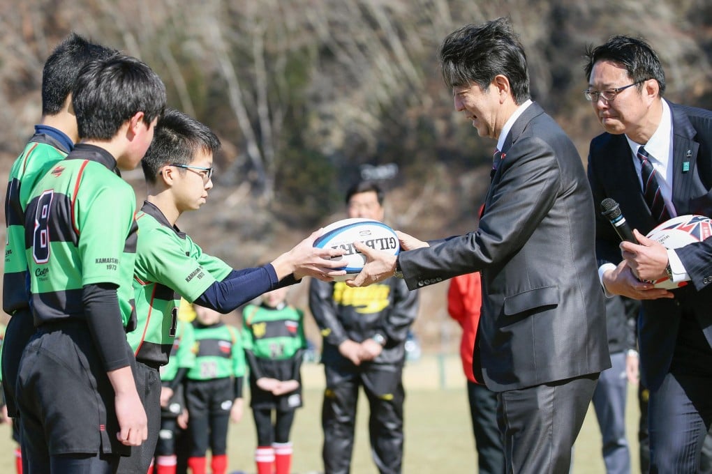 Japanese Prime Minister Shinzo Abe (second right) hands an autographed rugby ball to a child at the newly built Kamaishi Recovery Memorial Stadium, one of the stadiums to be used for the Rugby World Cup. Photo Kyodo