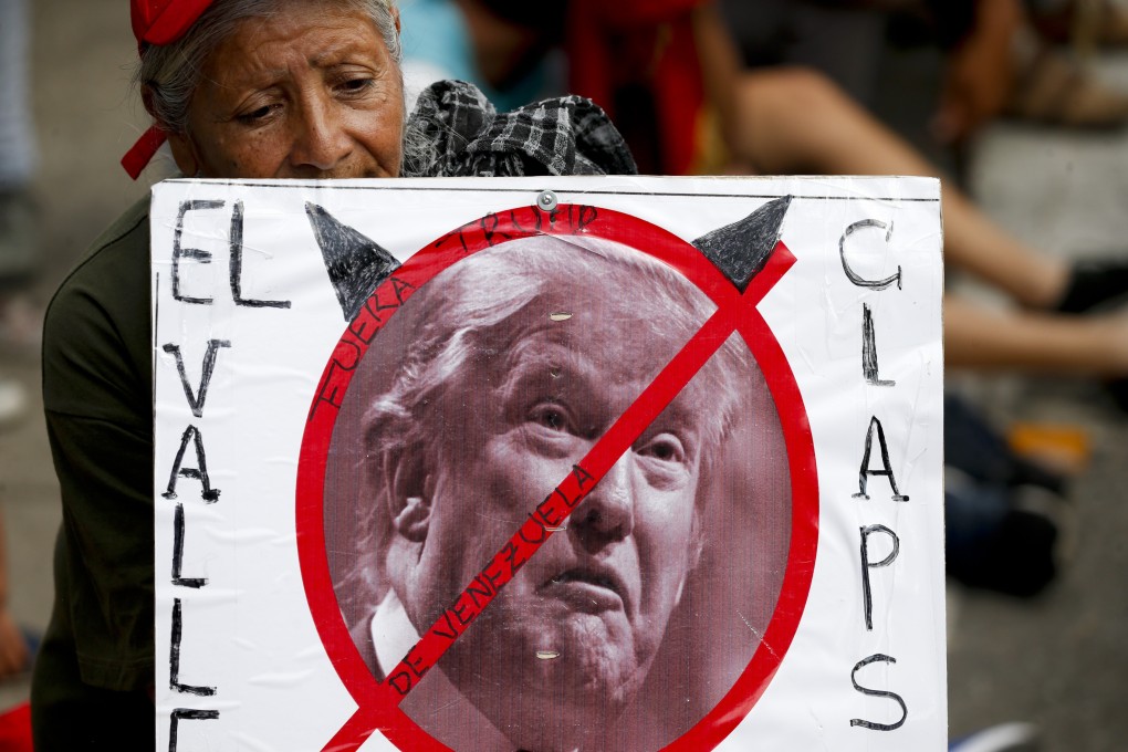 A government supporter holds a poster of US President Donald Trump defaced with devil horns, and a message that reads in Spanish: “Stay out Venezuela Trump,”. Photo: AP Photo