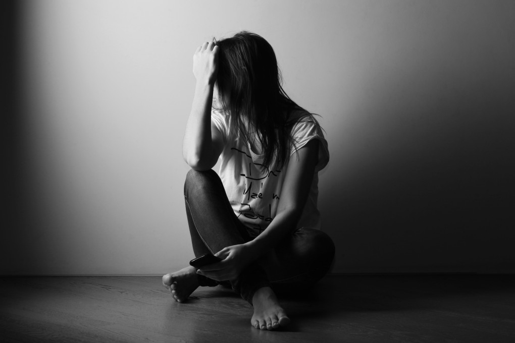 Teenager girl with depression sitting alone on the floor in the dark room. Black and white photo. Photo: Shutterstock