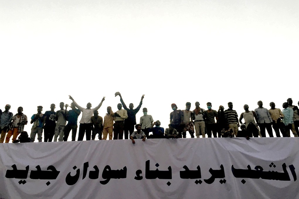 Demonstrators outside the military headquarters in Khartoum, stand above a banner reading in Arabic: ‘People want to build new Sudan’. Photo: Reuters