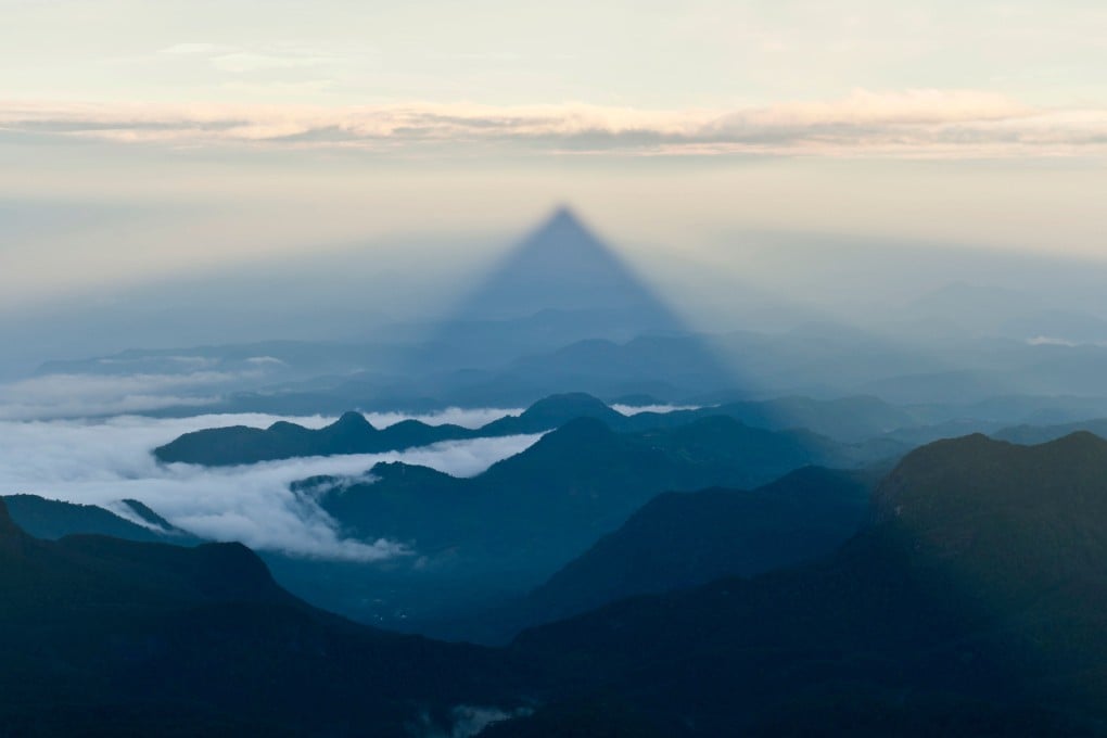At sunrise on Adam’s Peak, or Sri Pada, in Sri Lanka, the triangular shadow of the mountain is projected across the forest and countryside in the distance. Photo: Alamy