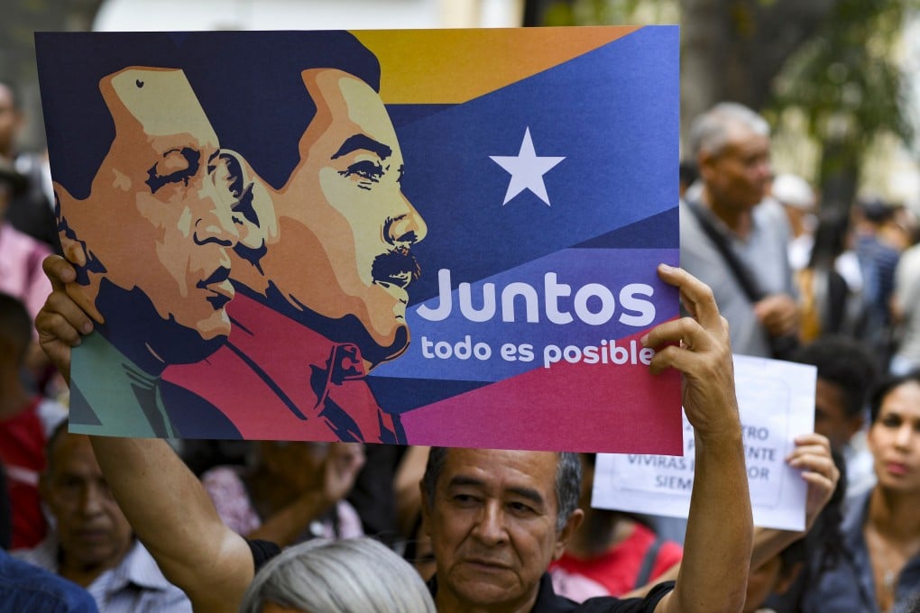 A government supporter raises a poster with images of Venezuela´s late president Hugo Chavez (left) and President Nicolas Maduro during a rally at Bolivar square in Caracas, Venezuela, on April 12, 2019. Photo: AFP