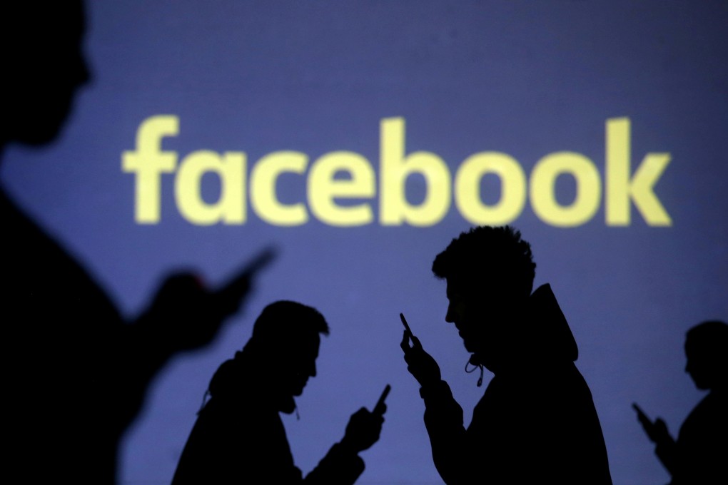 Silhouettes of mobile users are seen next to a screen projection of Facebook logo. Photo: Reuters