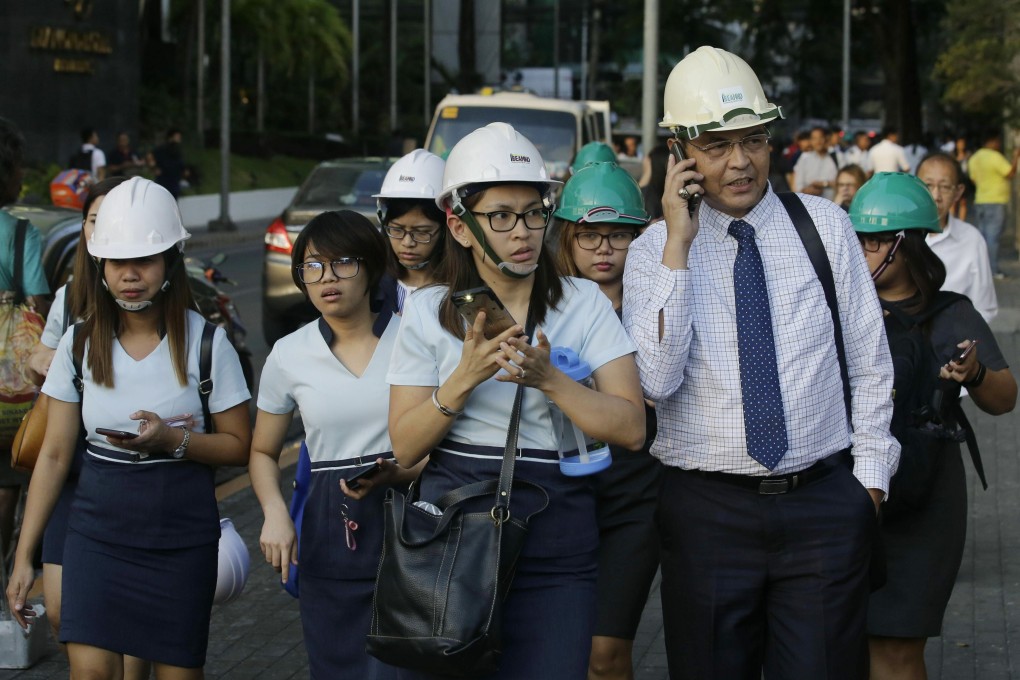 Wearing helmets, employees evacuate their building after an earthquake near Manila on Monday. Photo: AP