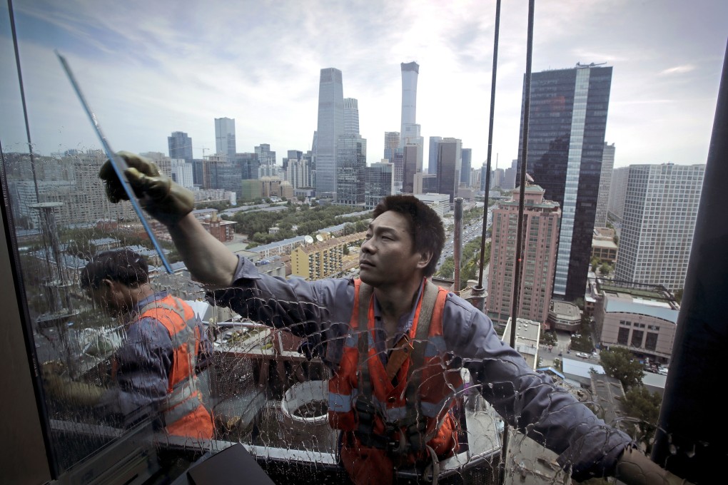 Workers on a suspended platform clean the windows of an office building in Beijing’s main business area. Photo: AP