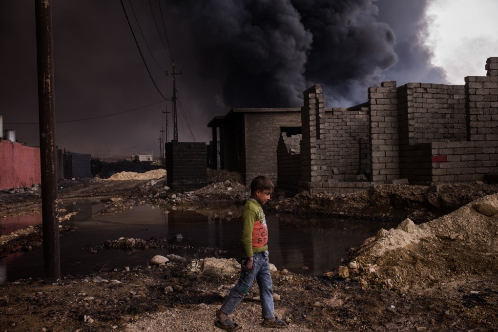A boy walks through a street near his home in Qayyarah, Iraq, on November 10, 2016, as an oil well burns nearby. Many streets and neighbourhoods in Qayyarah at the time looked apocalyptic, yet children could still be seen everywhere playing outside. Photo: Nicole Tung