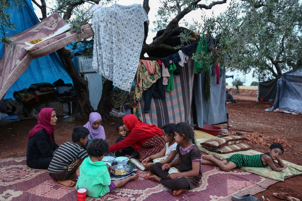 Displaced Syrian mother Mona Mutayr (centre, wearing a red shawl) breaks her fast with her children in a field near a camp for displaced people at the village of Atme, in the jihadist-held northern Idlib province. Photo: AFP
