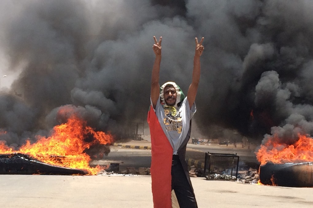 A protester flashes the victory sign in front of burning tires and debris, near Khartoum's army headquarters. Photo: AP