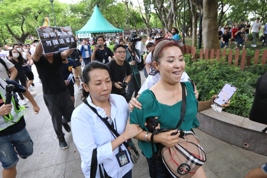 An officer escorts a woman away from angry protesters in Tuen Mun Park who are decrying niosy and indecent performances by ‘dama’ entertainers, mostly mainlanders. Photo: Felix Wong