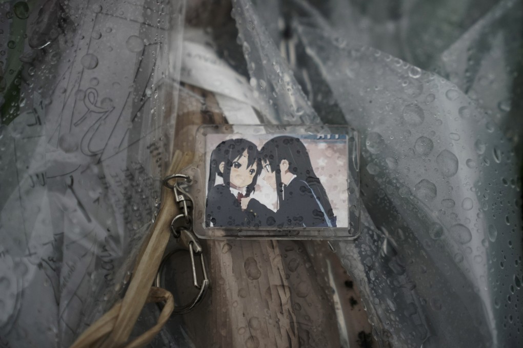 A keychain with a cartoon image is placed on top of flowers placed near the Kyoto Animation Studio building destroyed in an attack Friday. Photo: AP