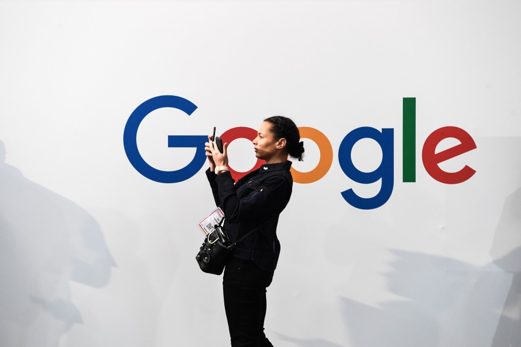 A woman takes a picture with two smartphones in front of the Google logo. Photo: AFP