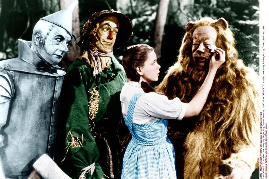 Classic American Films: The Wizard of Oz. Dorothy comforts the Cowardly Lion while the Tin Man and The Scarecrow look on.