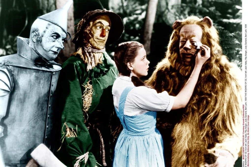Classic American Films: The Wizard of Oz. Dorothy comforts the Cowardly Lion while the Tin Man and The Scarecrow look on.