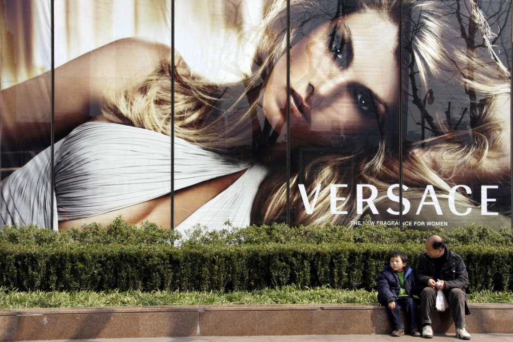 A man and a child sit in front of a Versace advertisement in Shanghai in February 2008. Photo: AP