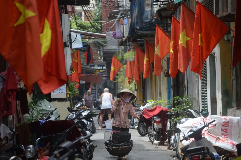 A street vendor walking past rows of Vietnamese national flags hung in front of homes for Vietnam's National Day in downtown Hanoi. Photo: AFP