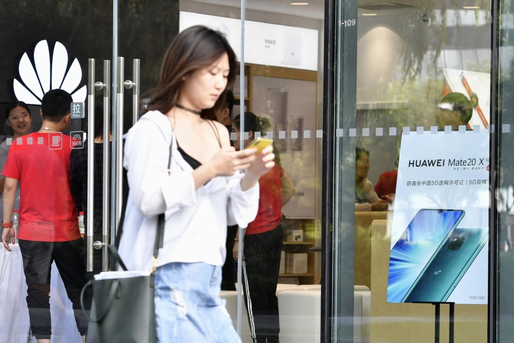 A woman checks her phone as she walks by a Huawei store in Beijing. Photo: Kyodo