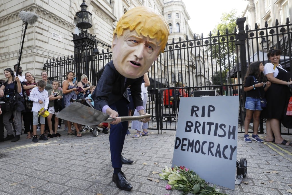 A man in a giant Boris Johnson ‘head’ digs a grave at the foot of a pretend tombstone outside Downing Street in London. Photo: AP