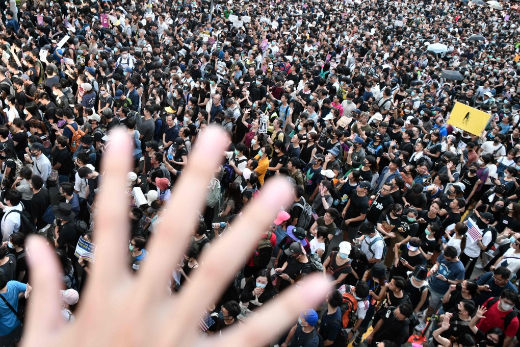 A man holds up his hand to symbolise the five demands of Hong Kong protesters as demonstrators protest in the background. Photo: AFP