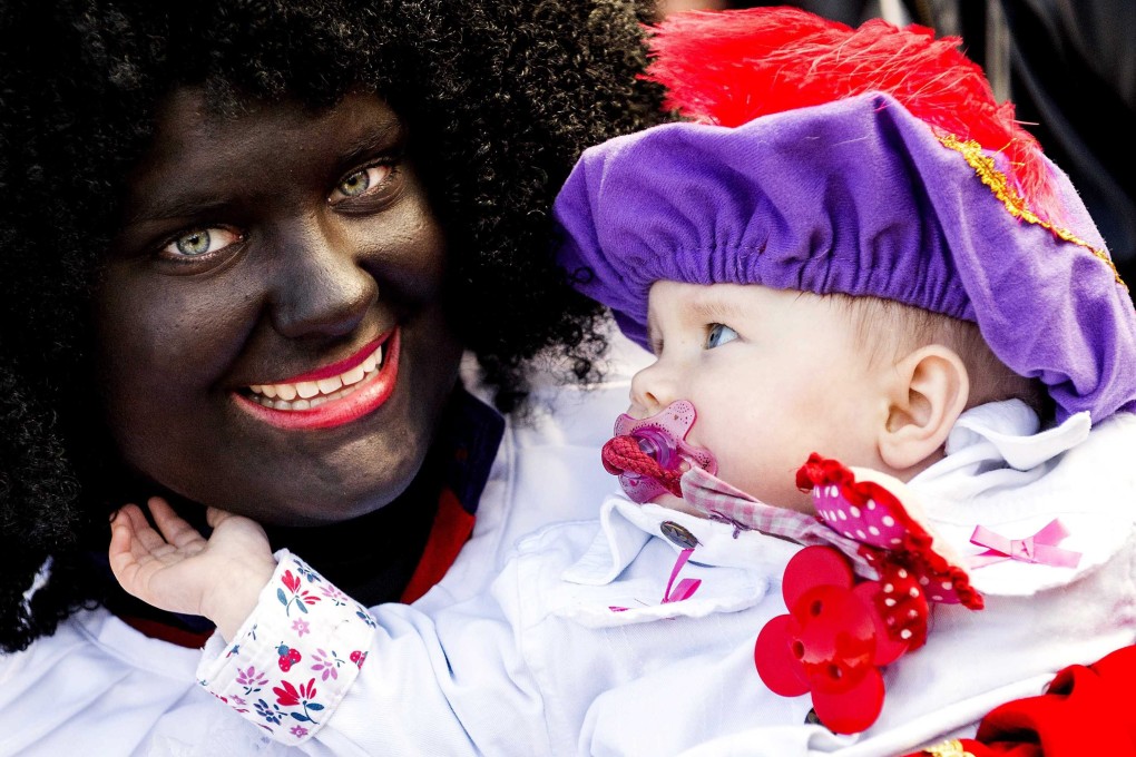 A woman dressed as Zwarte Piet (Black Pete) holds a baby at a park The Hague, The Netherlands. Photo: EPA