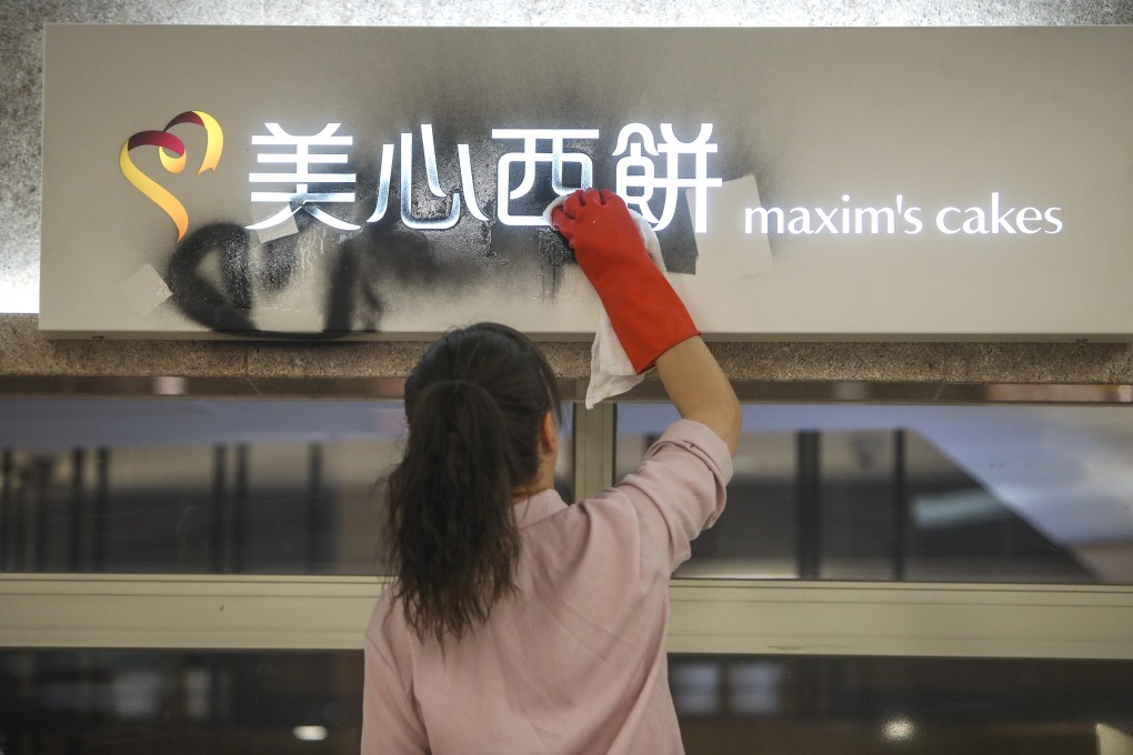 An employee tries to remove graffiti from a sign at a Maxim's cake shop in New Town Plaza in Sha Tin. Photo: Winson Wong