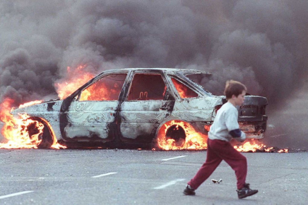 A boy runs past a burning car in the Catholic area of Shortstrand during the Troubles in Belfast, Northern Ireland in July 1996. Photo: AFP