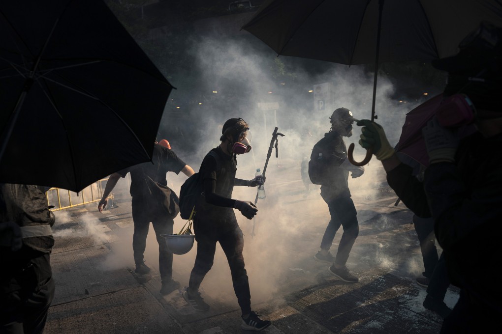 Black-clad protesters stand surrounded by smoke from tear gas canisters in Hong Kong. Photo: AP