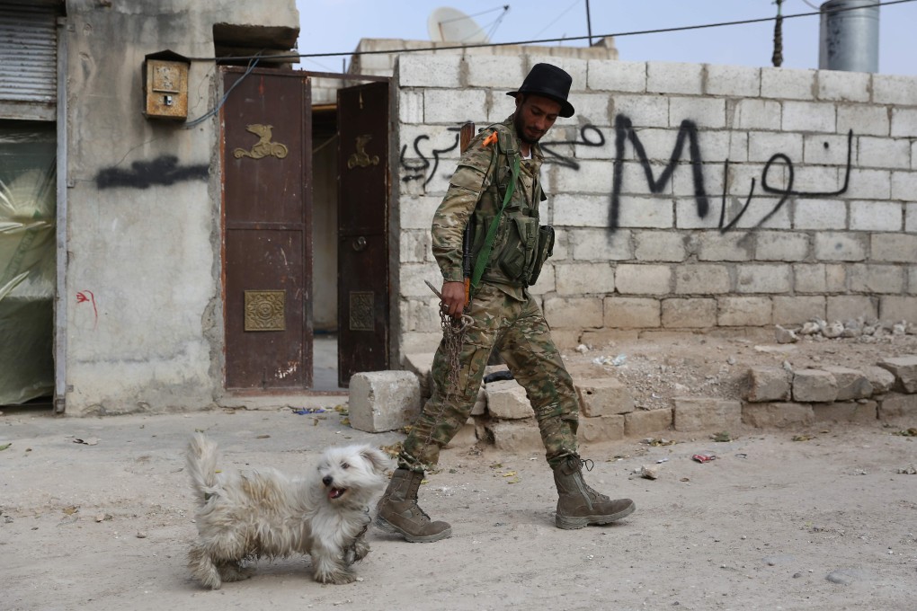 A Turkey-backed Syrian fighter plays with a dog in the Syrian border town of Ras al-Ain. Photo: AP