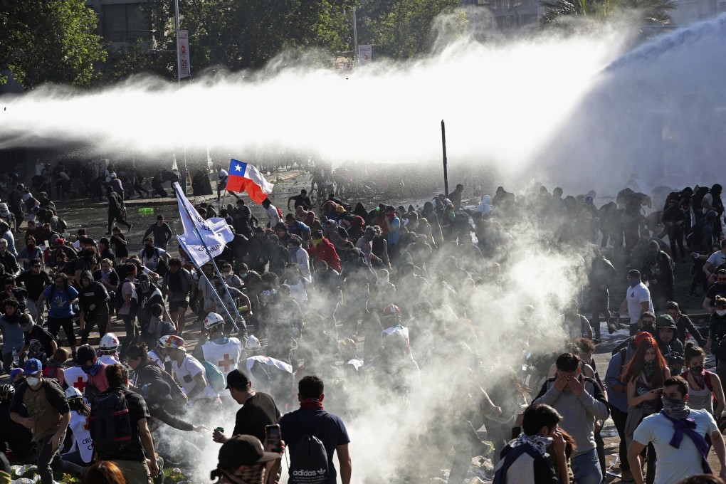Demonstrators run from police launching water canons and tear gas as a state of emergency remains in effect in Santiago, Chile. Photo: AP