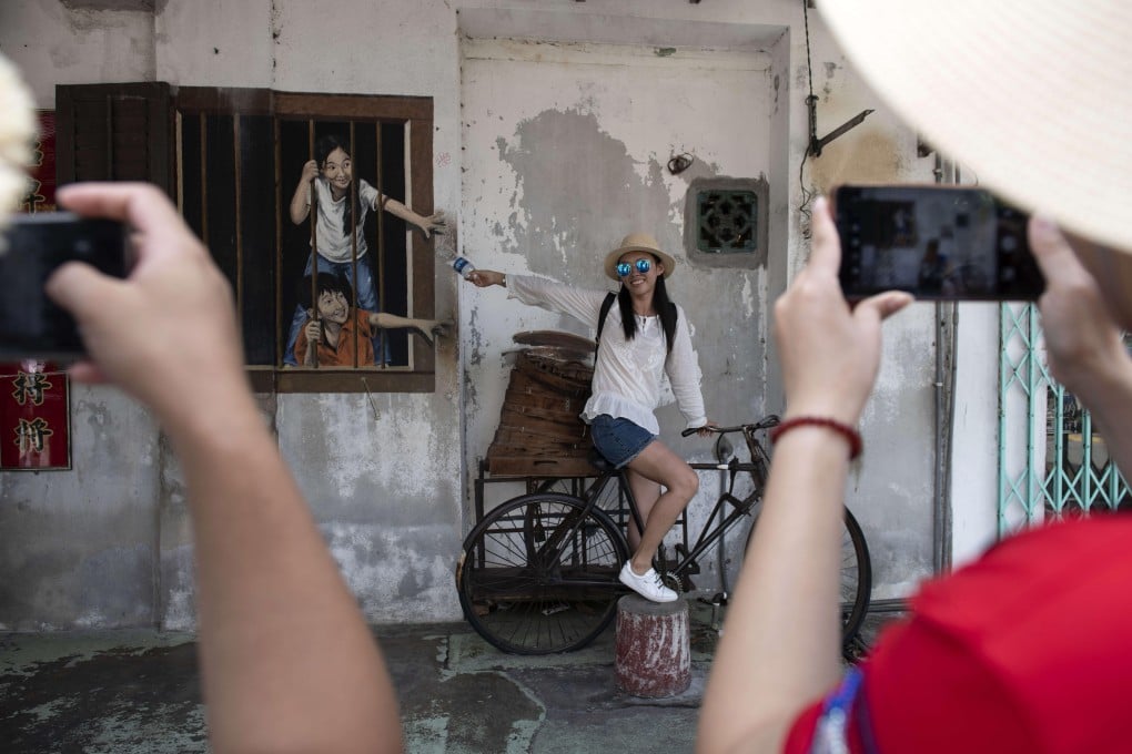 Tourists taking photos on George Town’s Armenian Street with a mural called I Want Bao by Kuala Lumpur-born artist WK Setor on the side wall of a pastry shop. Photo: Alamy