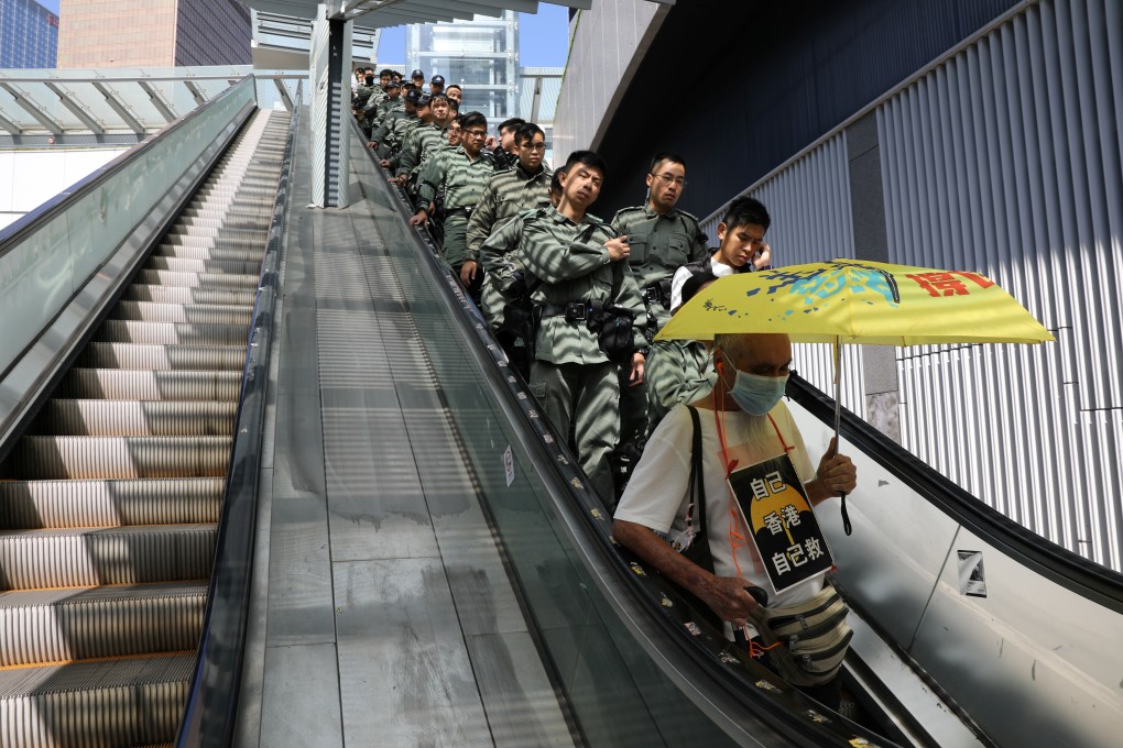 A line of police officers rides an escalator behind a protester wearing a placard which reads: “Hong Kong is ours, save it ourselves”, ahead of Chief Executive Carrie Lam’s annual policy address on October 16, as anti-government protests entered their fifth month. Photo: Reuters