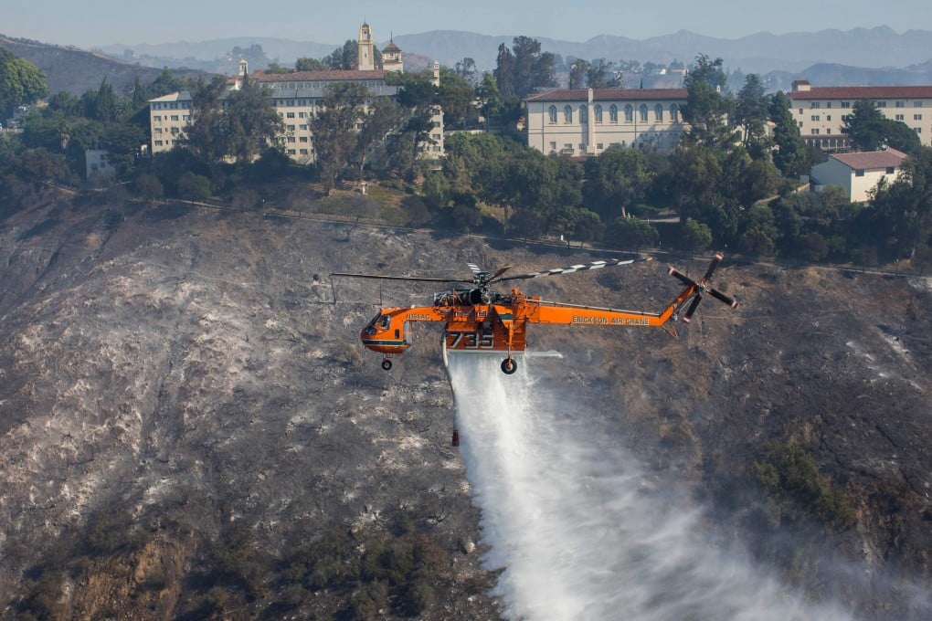 A helicopter drops water on houses as the Getty fire burns in the Brentwood area, California. Photo: AFP