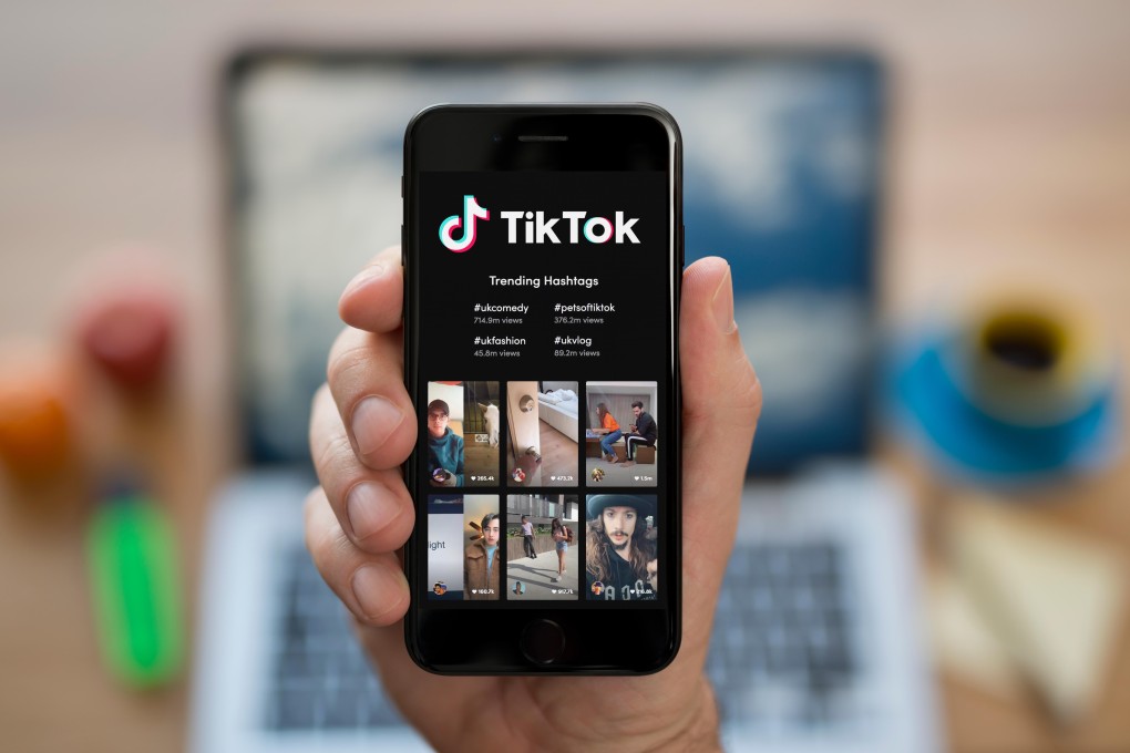 A man looks at his iPhone which displays the Tik Tok logo