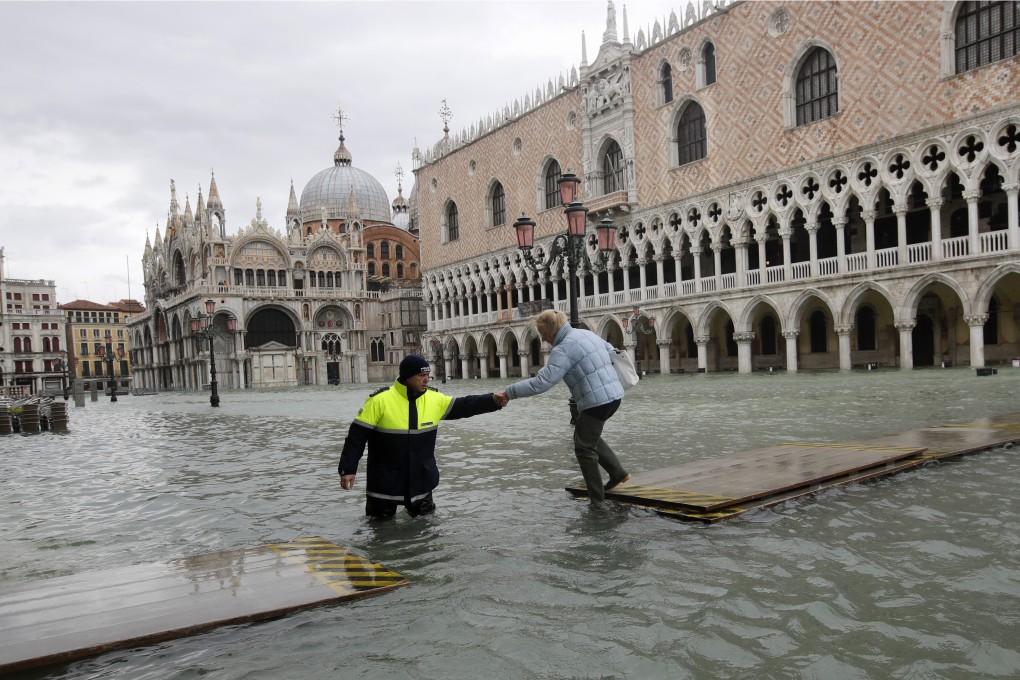 A city worker helps a woman who decided to cross St Mark’s square in Venice on a gangway, in spite of prohibition. Photo: AP