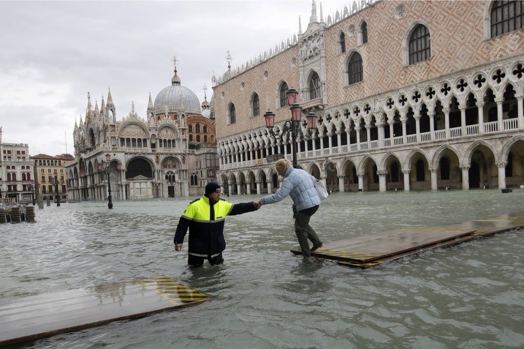 A city worker helps a woman who decided to cross St Mark’s square in Venice on a gangway, in spite of prohibition. Photo: AP