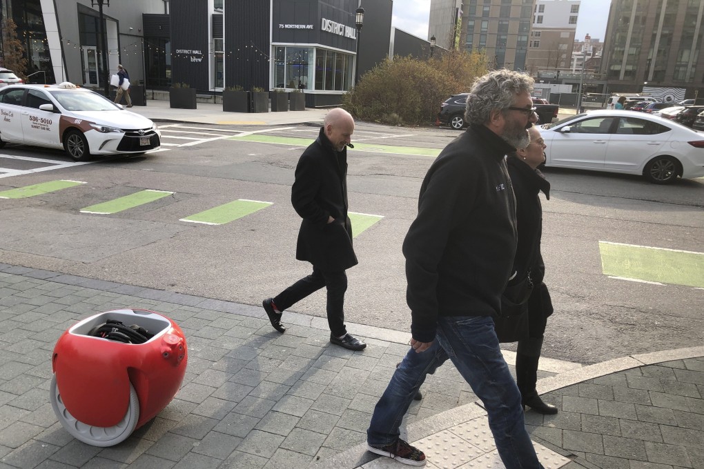 Piaggio Fast Forward chief executive Greg Lynn, centre, is followed by his company's Gita carrier robot, as he crosses a street on November 11 in Boston. The two-wheeled machine is carrying a backpack and uses cameras and sensors to track its owner. Photo: AP