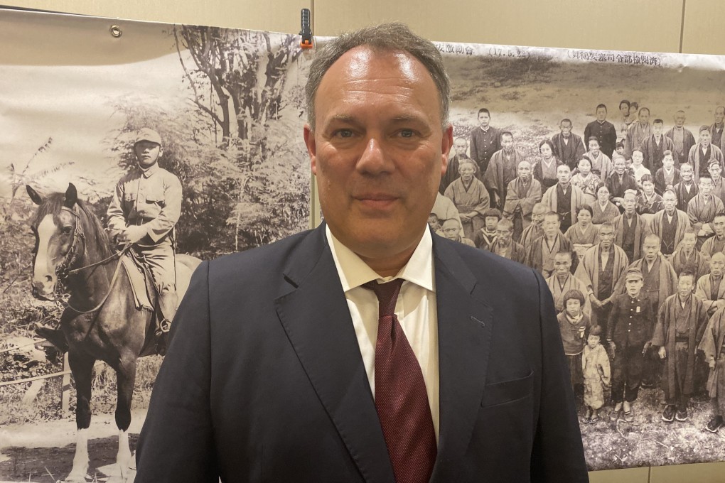 Dr Jarat Chopra stands in front of an image of Hideo Shikata on a horse, as well as a group photo of villagers from Maizuru. Photo: Julian Ryan