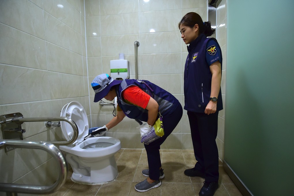 A member of Seoul city’s “hidden camera-hunting” squad and a policewoman inspect a women’s bathroom stall. Photo: AFP