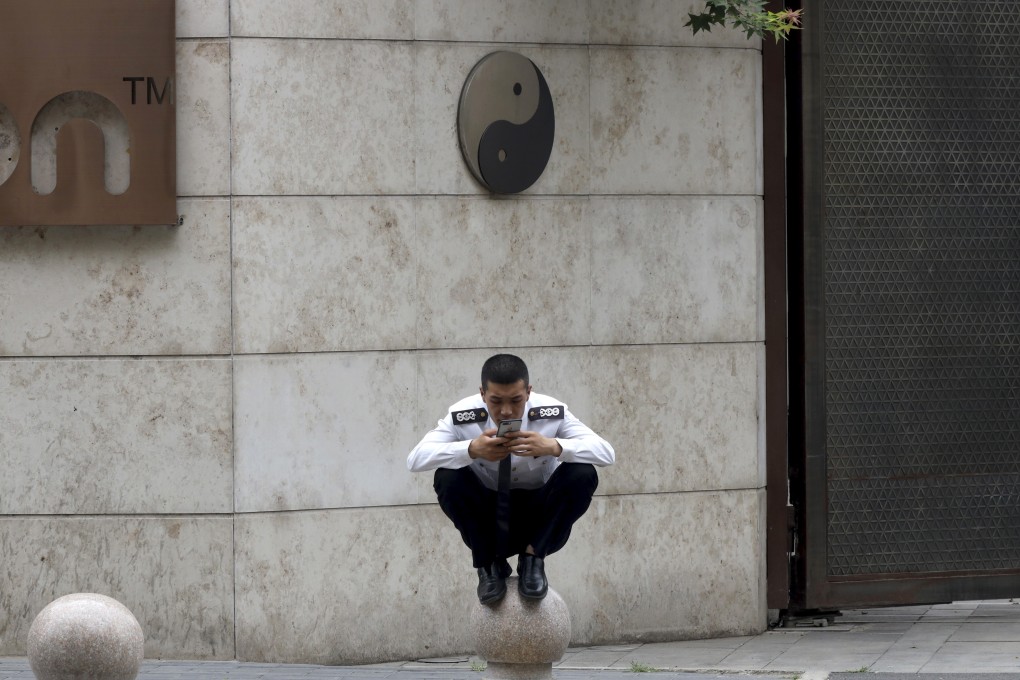 A security guard looks at his mobile phone while perched on a barrier near a yin and yang symbol in Beijing. The symbol is rooted in ancient Chinese philosophy and represents harmony. Photo: AP