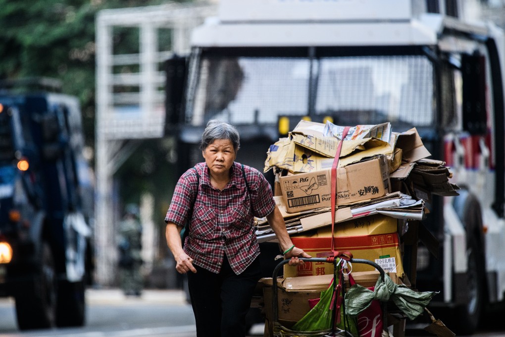 An elderly woman drags a trolley load of cardboard for recycling in front of a police water cannon vehicle in Hong Kong. Photo: AFP