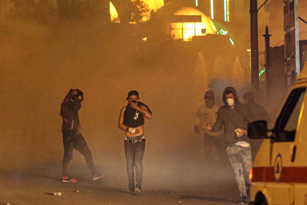 Protesters flee gas grenades after they threw stones at riot police during clashes in central Beirut. Photo: EPA-EFE