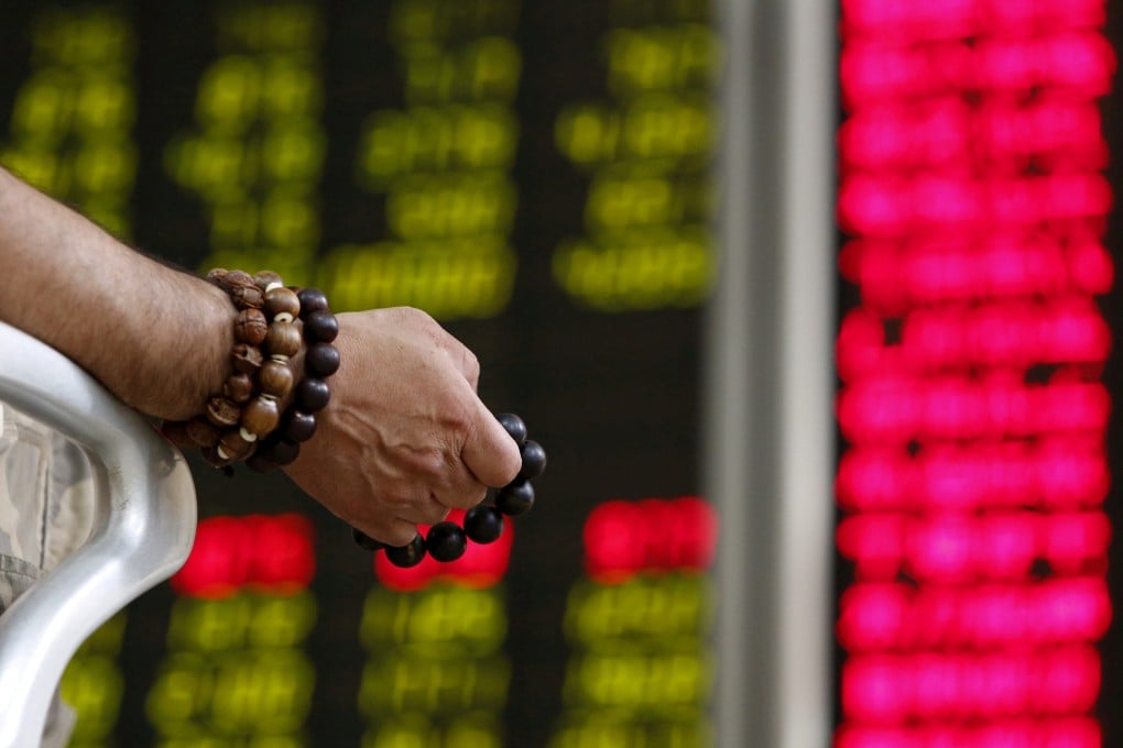 An investor holds onto prayer beads as he watches a board showing stock prices at a brokerage office in Beijing. Photo: Reuters