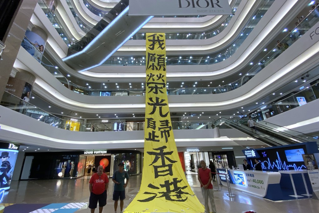 Protesters unfurl a banner inside the Times Square shopping mall, where the Louis Vuitton store (left, in the background) is expected to close because of the impact of protests on tourism and luxury retail sales. The mall has often been targeted by protesters and stores have been forced to close early. Photo: Robert Ng