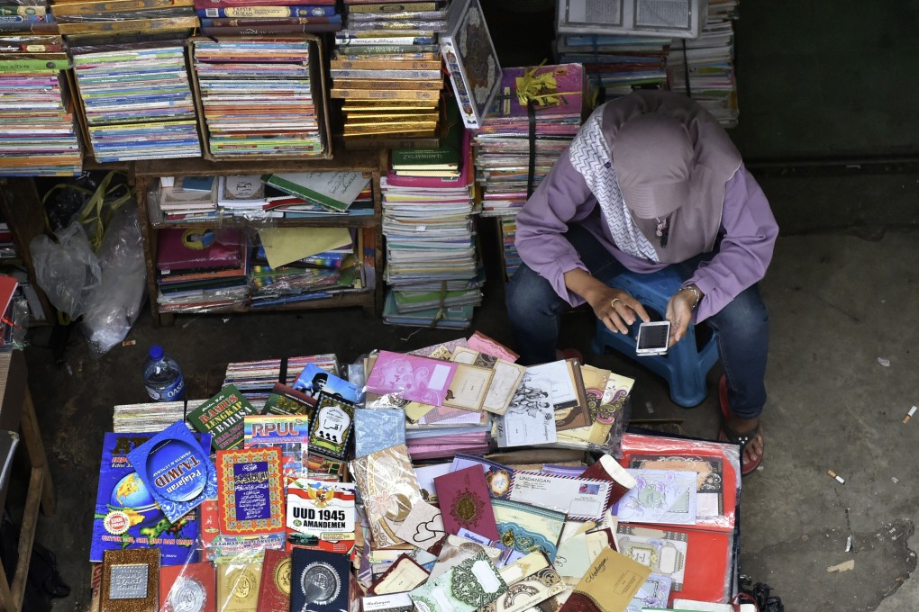 A book vendor in Jakarta uses her mobile phone while waiting for customers. Indonesia has one of the fastest growing internet penetration rates in the region. Photo: AFP