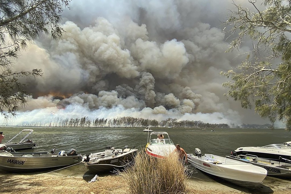 Boats are pulled ashore as smoke and wildfires rage behind Lake Conjola, Australia on Thursday. Photo: AP