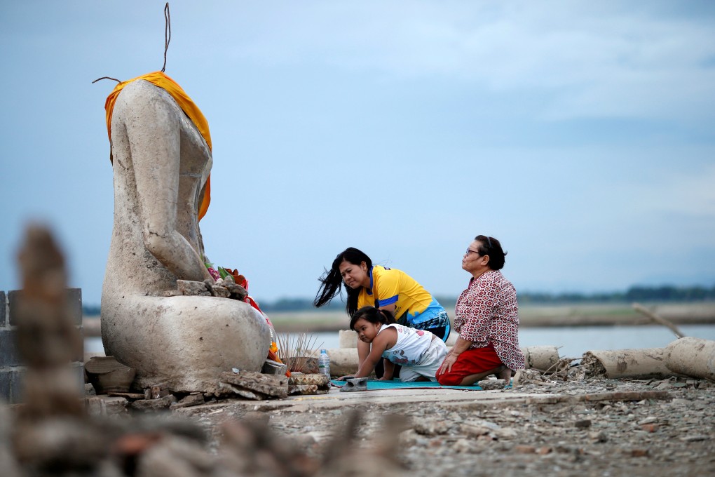 A family prays near a headless Buddha statue, which resurfaced in a dried-up dam in Lopburi, Thailand, due to drought. Photo: Reuters
