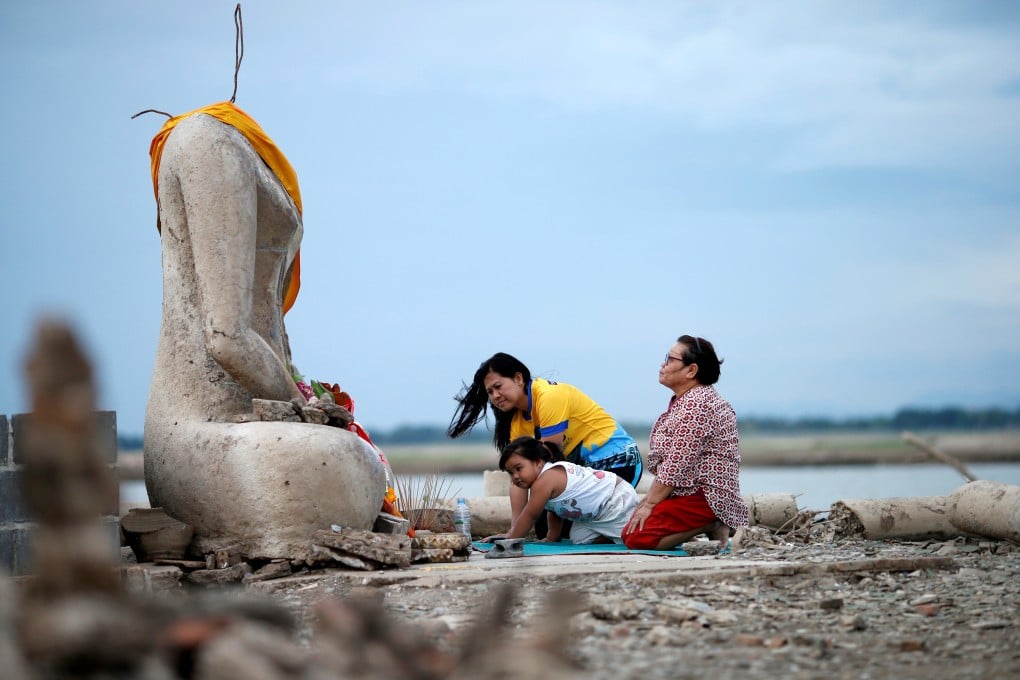 A family prays near a headless Buddha statue, which resurfaced in a dried-up dam in Lopburi, Thailand, due to drought. Photo: Reuters