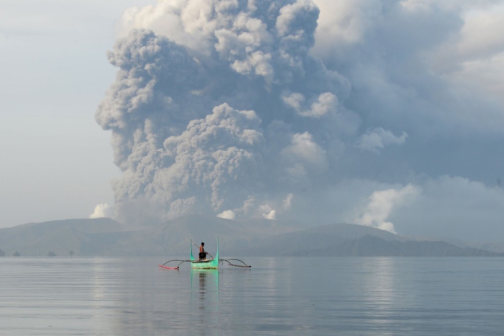 A youth steers a canoe while the volcano spews ash behind him. The Philippines is on alert for an ‘explosive eruption’ of the volcano south of Manila. Photo: AFP