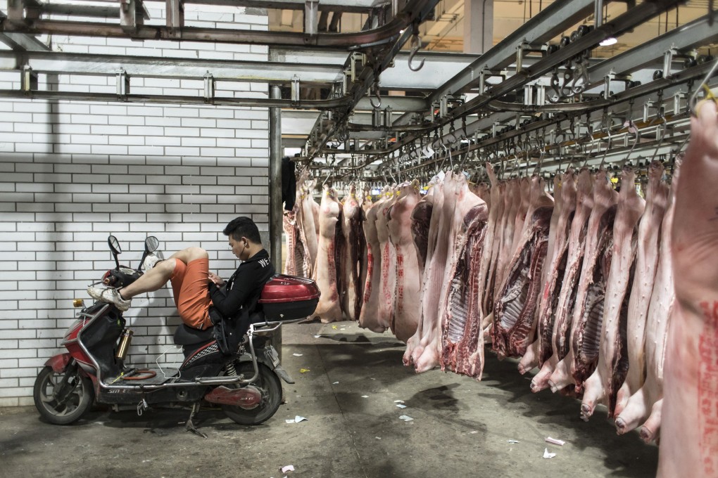 A man sits on a motorcycle next to pig carcasses hanging from a conveyor at a pork wholesale market on the outskirts of Shanghai on May 28, 2019. The US pork industry has been hard hit by Chinese tariffs during the trade war. Photo: Bloomberg