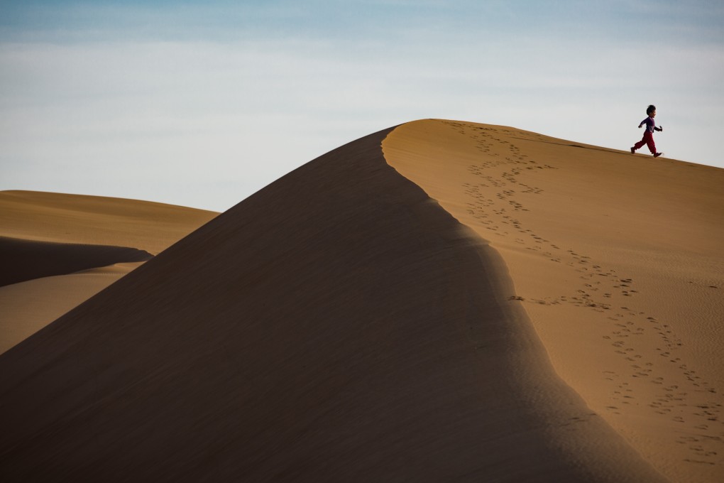 A view from the home of the family of Du Jinping, 45, who lives in China’s Tengger Desert, of her daughter Liu Jiali running through sand dunes. The family are among “ecological migrants” forced to move home by desertification. Photo: Josh Haner/The New York Times