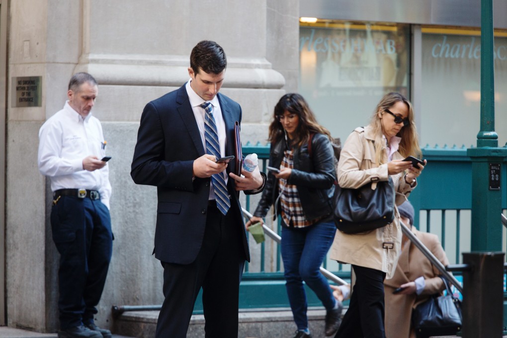 Pedestrians check their smartphones on Wall Street in New York in November 2018. The increasing popularity of phone apps means that tech firms, including those with ties abroad, have access to vasts amounts of user data. Photo: Bloomberg